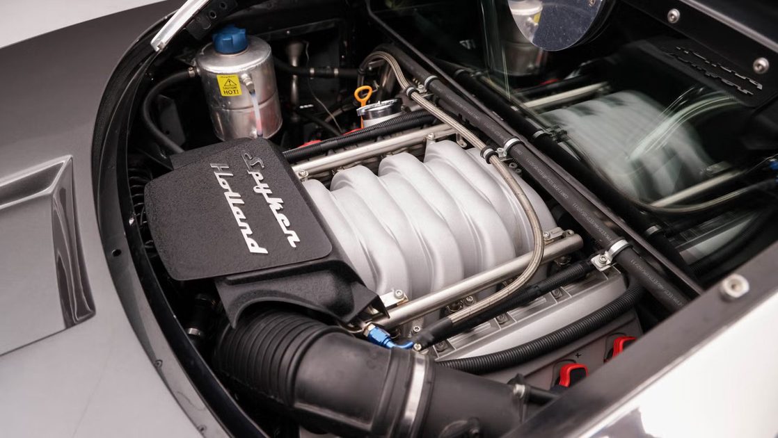 rear three quarter view mid engine bay with exposed intake manifold hoses and metallic components under glass cover.
