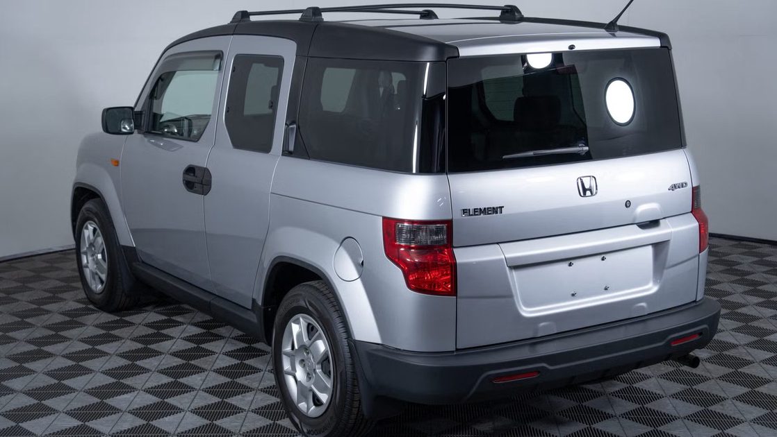 rear three quarter view of silver boxy suv with tailgate glass, rear lights, roof rails.