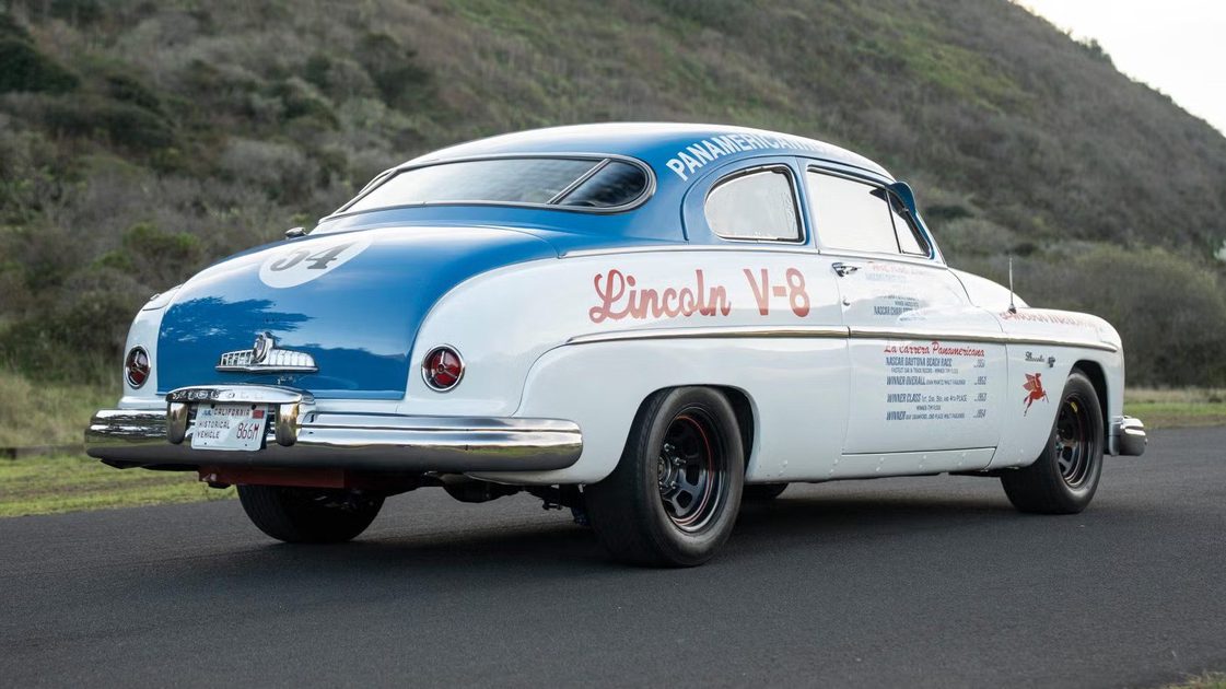 rear three quarter view of vintage race coupe with racing decals parked on road.