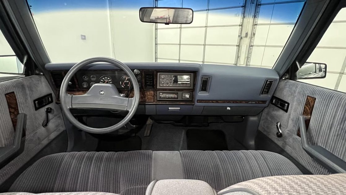 vehicle interior showing steering wheel analog gauges center radio controls bench seat cloth upholstery dashboard.