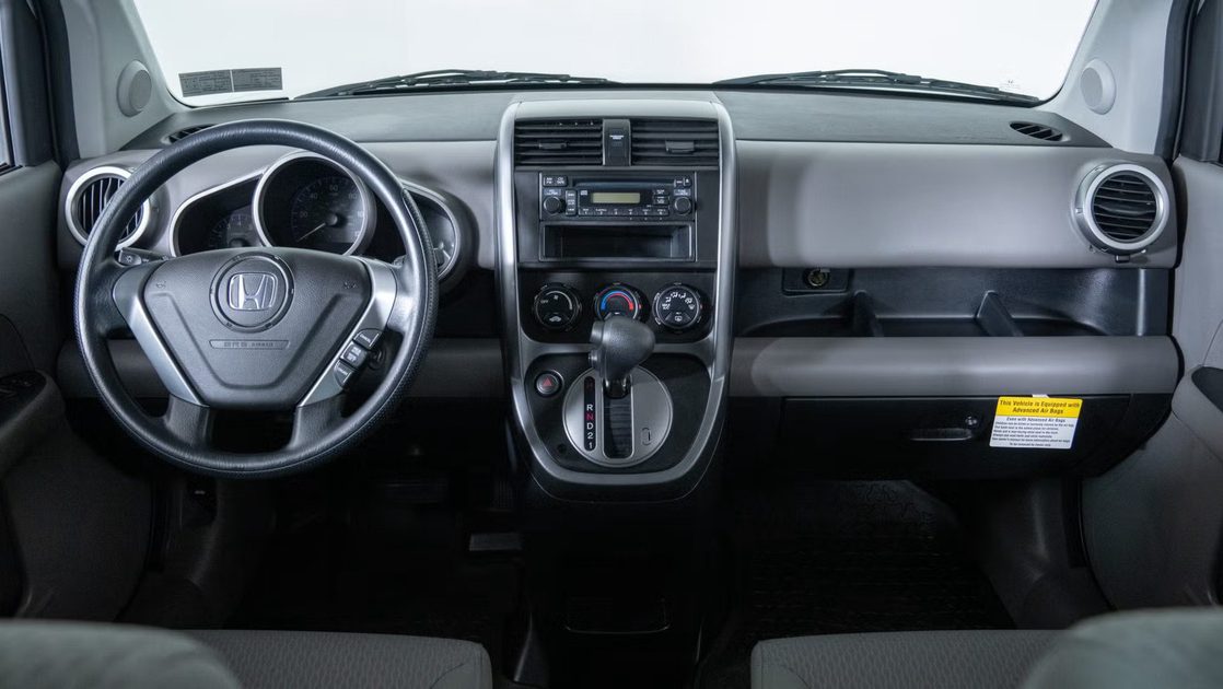 vehicle interior with steering wheel, analog gauges, center vents, radio controls, automatic gear shifter.