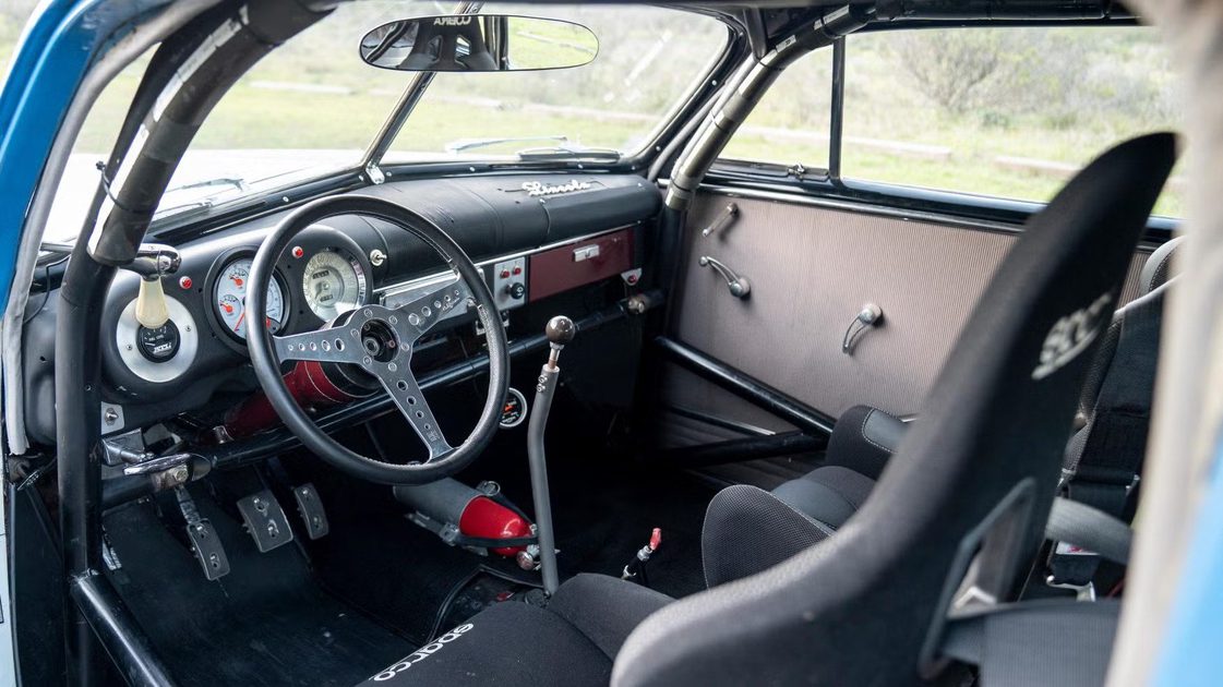 vehicle interior with steering wheel, analog gauges, manual gear shifter, racing seat.