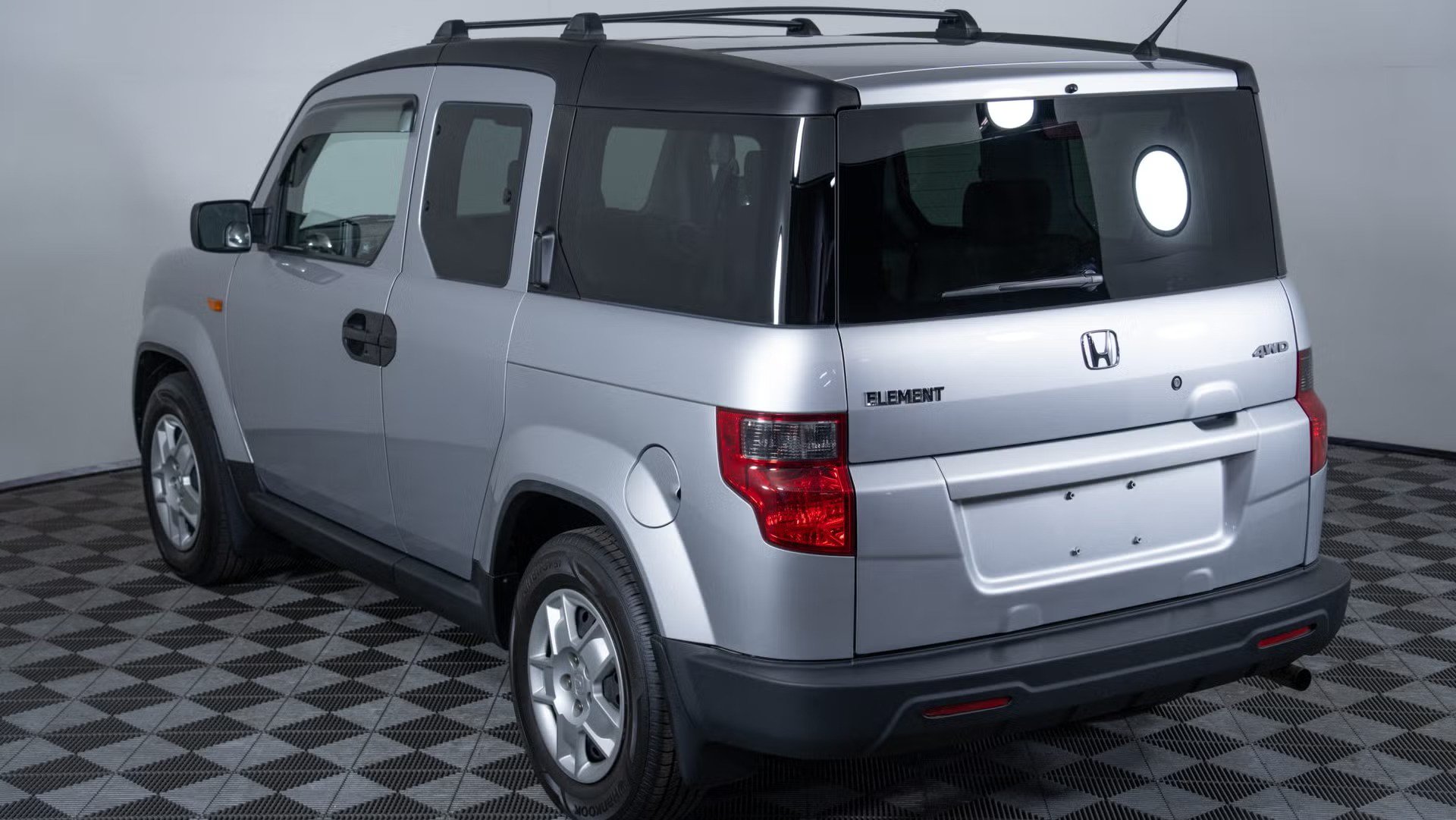 rear three quarter view of silver boxy suv with tailgate glass, rear lights, roof rails.