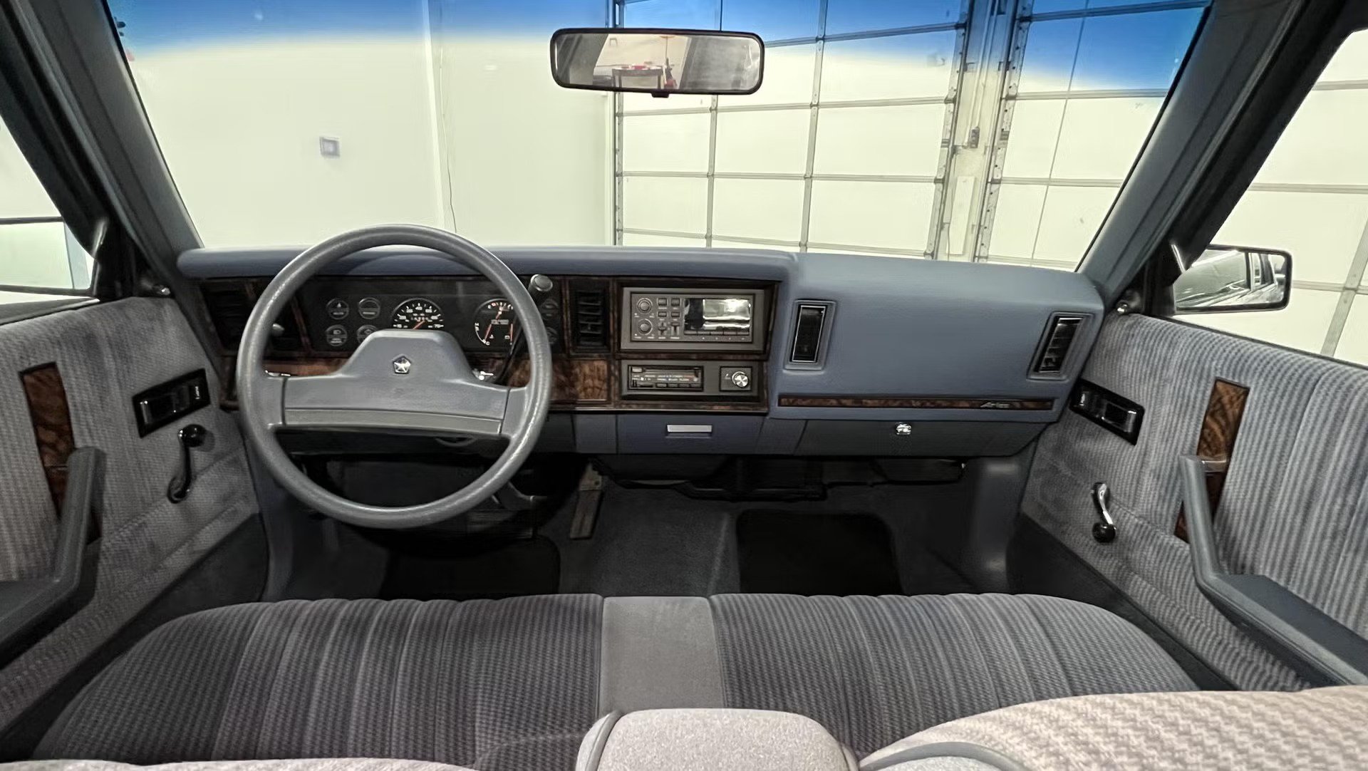 vehicle interior showing steering wheel analog gauges center radio controls bench seat cloth upholstery dashboard.