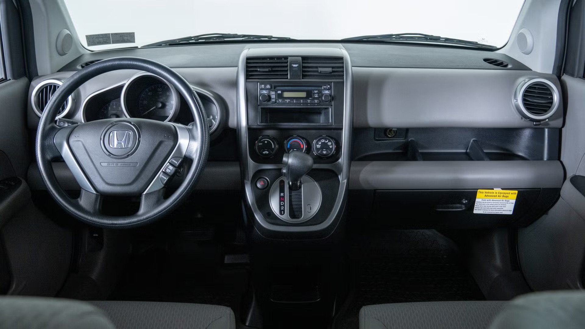 vehicle interior with steering wheel, analog gauges, center vents, radio controls, automatic gear shifter.